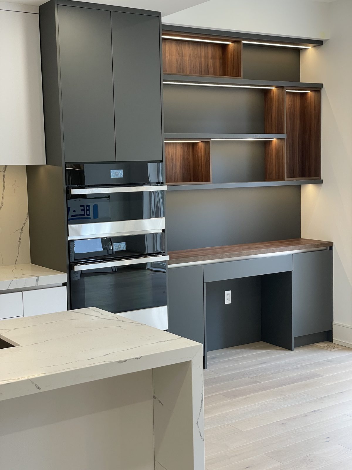 Built-in oven tower with walnut desk niche and niche lighting — Berm Inc. project photo